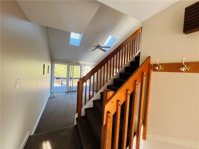 stairs with a skylight, ceiling fan, carpet floors, and high vaulted ceiling