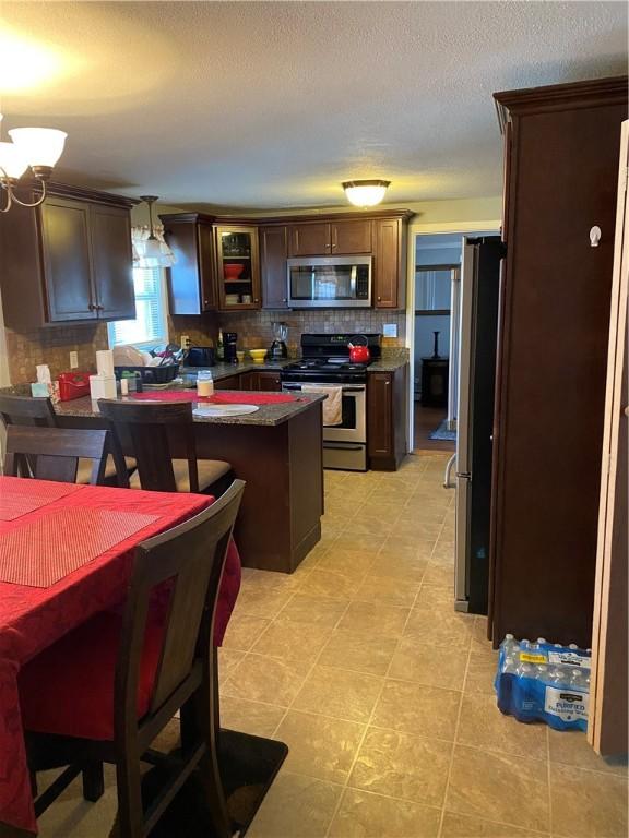 kitchen with stainless steel appliances, a peninsula, dark brown cabinets, decorative backsplash, and dark countertops