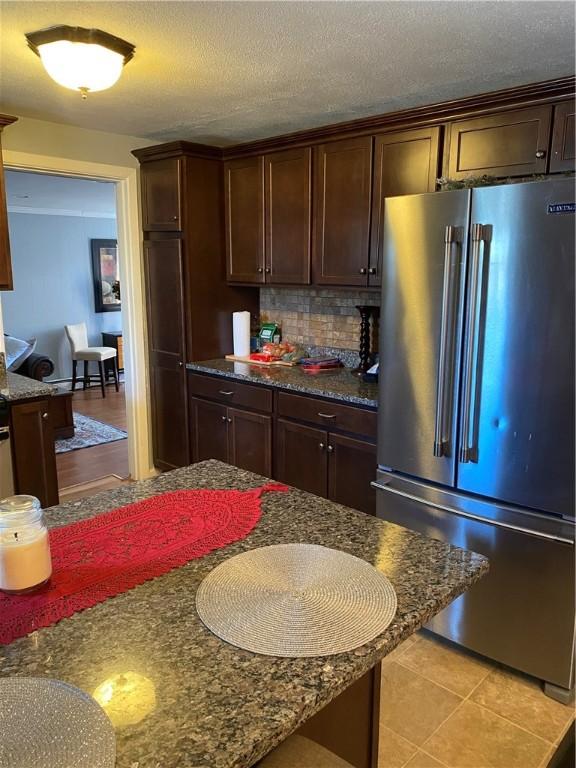 kitchen with light tile patterned floors, backsplash, high quality fridge, a textured ceiling, and dark brown cabinets