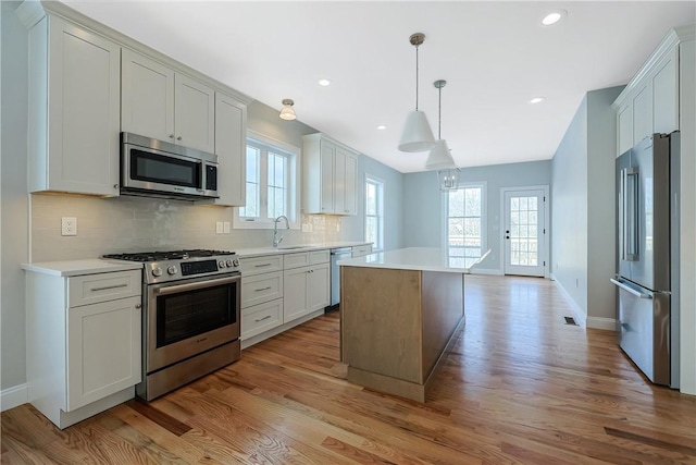 kitchen featuring pendant lighting, appliances with stainless steel finishes, white cabinets, a kitchen island, and decorative backsplash