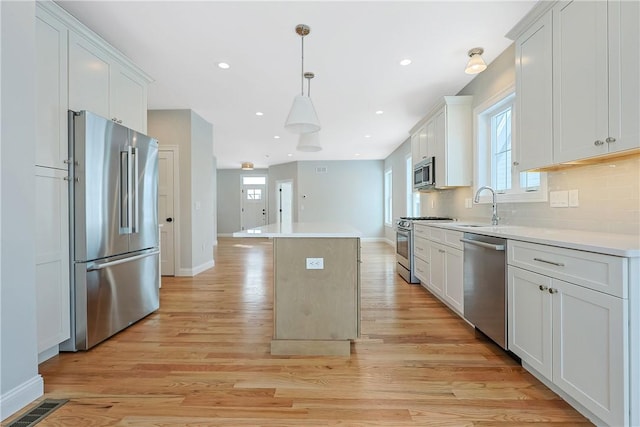 kitchen featuring pendant lighting, sink, stainless steel appliances, white cabinets, and a kitchen island