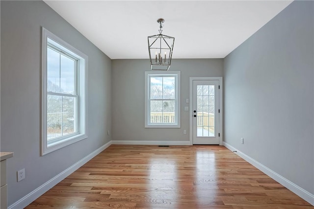 doorway to outside with a notable chandelier and light wood-type flooring