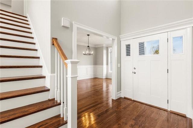 foyer entrance featuring dark hardwood / wood-style flooring, ornamental molding, and an inviting chandelier