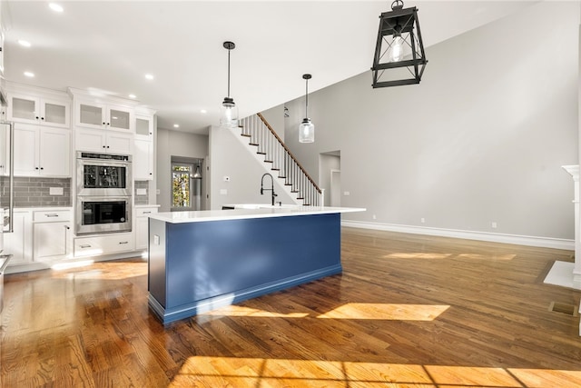 kitchen with double oven, backsplash, pendant lighting, a center island with sink, and white cabinets