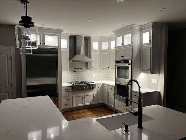 kitchen with white cabinetry, wall chimney range hood, light stone counters, dark hardwood / wood-style flooring, and appliances with stainless steel finishes