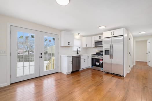 kitchen with french doors, light wood-type flooring, backsplash, stainless steel appliances, and white cabinetry