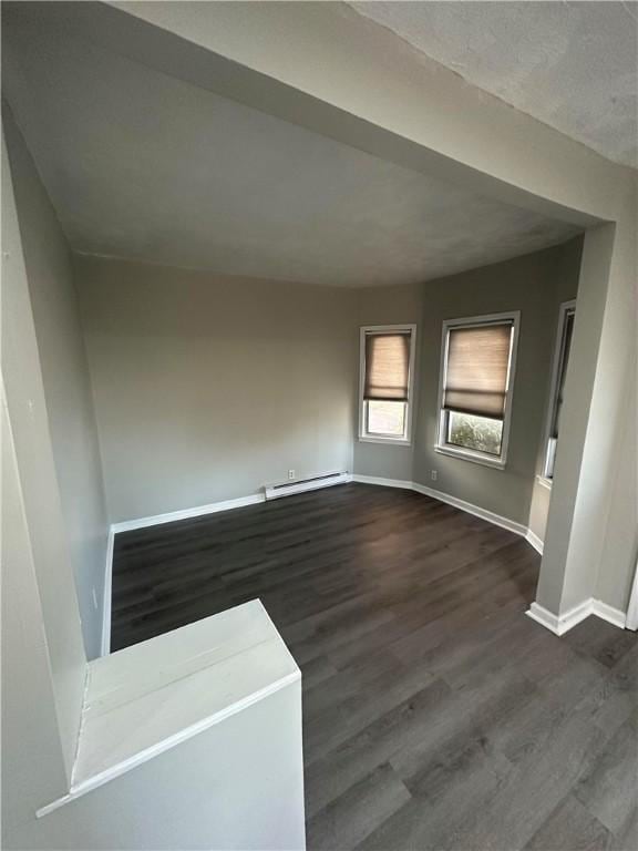 empty room with dark wood-type flooring and a baseboard heating unit