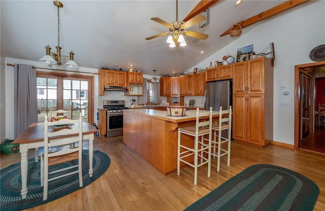 kitchen with pendant lighting, a center island, stainless steel appliances, vaulted ceiling with beams, and light wood-type flooring