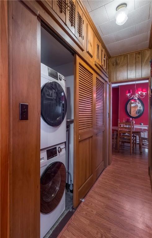 laundry area featuring wood-type flooring, stacked washer and dryer, and wooden walls