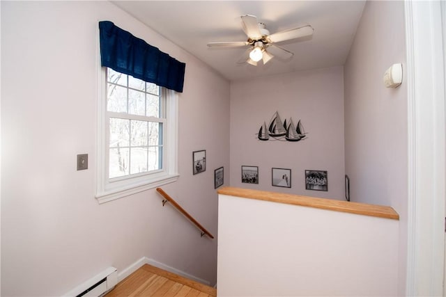 stairway featuring a baseboard heating unit, ceiling fan, and wood-type flooring