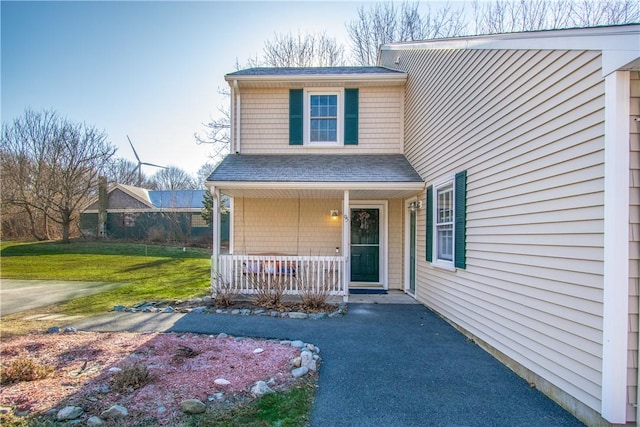 doorway to property featuring covered porch and a lawn