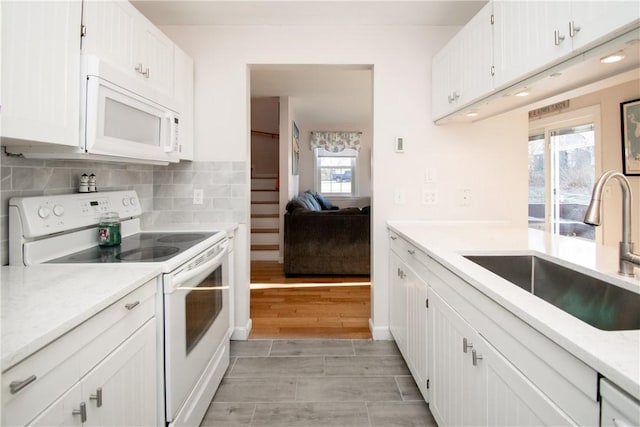 kitchen with backsplash, sink, white appliances, and white cabinetry