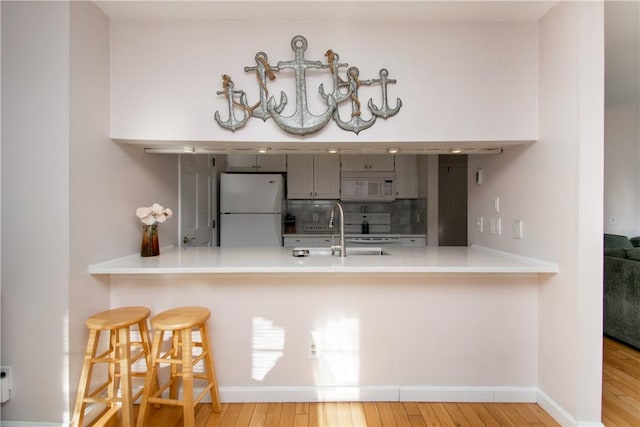 kitchen featuring kitchen peninsula, sink, white appliances, light hardwood / wood-style flooring, and a kitchen breakfast bar