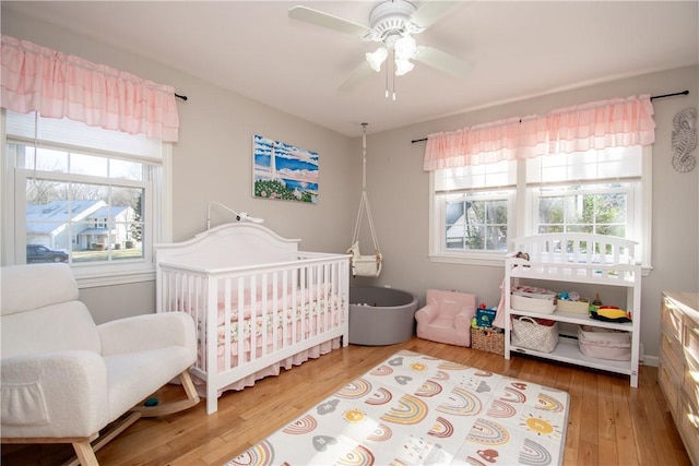 bedroom featuring ceiling fan, wood-type flooring, and a crib