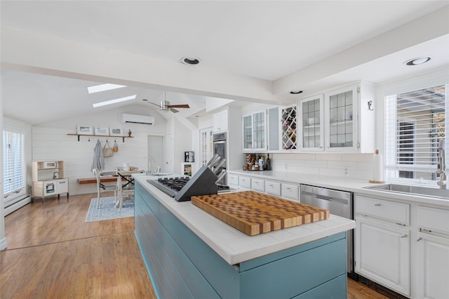 kitchen featuring vaulted ceiling with skylight, a wall mounted AC, a healthy amount of sunlight, white cabinets, and a kitchen island