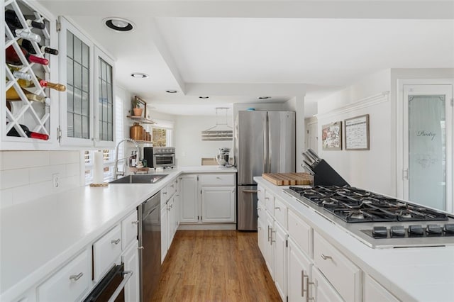 kitchen featuring tasteful backsplash, stainless steel appliances, sink, light hardwood / wood-style floors, and white cabinetry