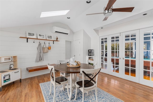 dining space with ceiling fan, french doors, light hardwood / wood-style flooring, an AC wall unit, and lofted ceiling with skylight