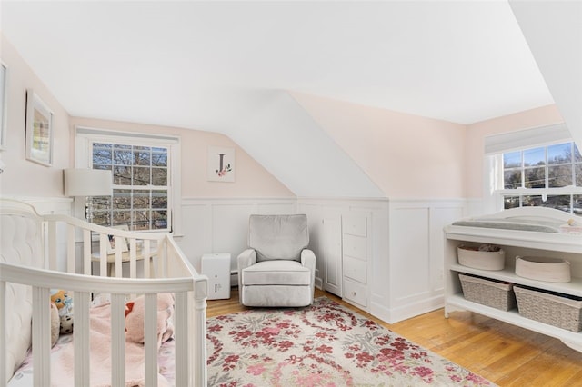 bedroom with lofted ceiling, light hardwood / wood-style floors, and a crib