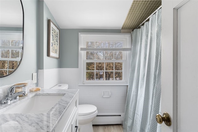 bathroom featuring vanity, baseboard heating, tile walls, hardwood / wood-style floors, and toilet