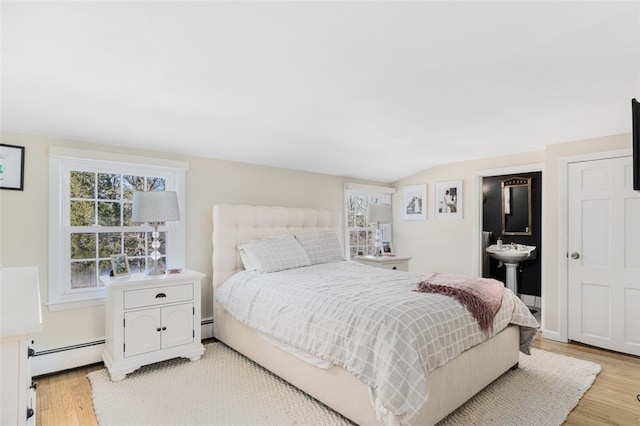 bedroom with light wood-type flooring, vaulted ceiling, a baseboard radiator, and ensuite bath