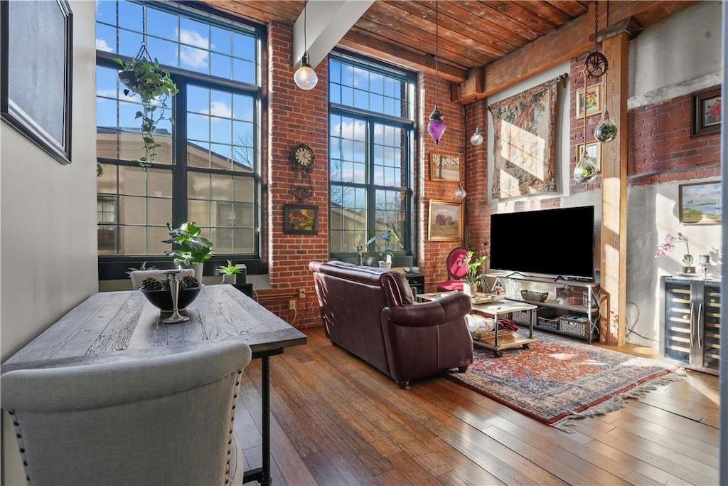 living room with a towering ceiling, brick wall, wood ceiling, wood-type flooring, and beam ceiling