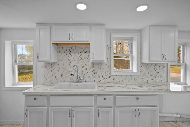 kitchen with decorative backsplash, white cabinetry, sink, and light stone counters