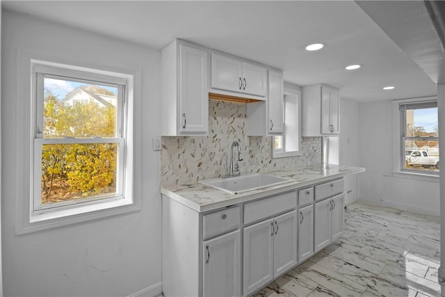 kitchen with a wealth of natural light, decorative backsplash, sink, and white cabinets