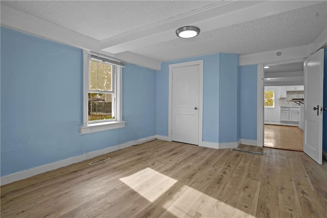 empty room with beamed ceiling, a textured ceiling, and light wood-type flooring