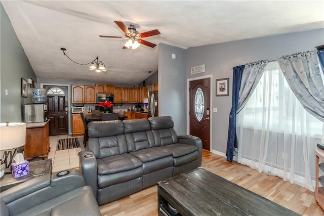 living room with light hardwood / wood-style floors, ceiling fan with notable chandelier, and vaulted ceiling