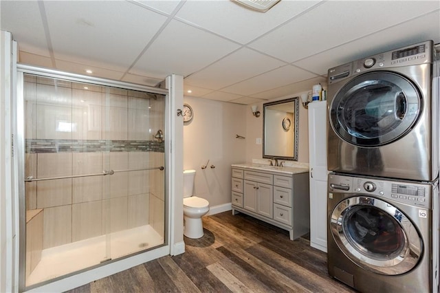 bathroom featuring wood-type flooring, an enclosed shower, stacked washer and clothes dryer, vanity, and a drop ceiling