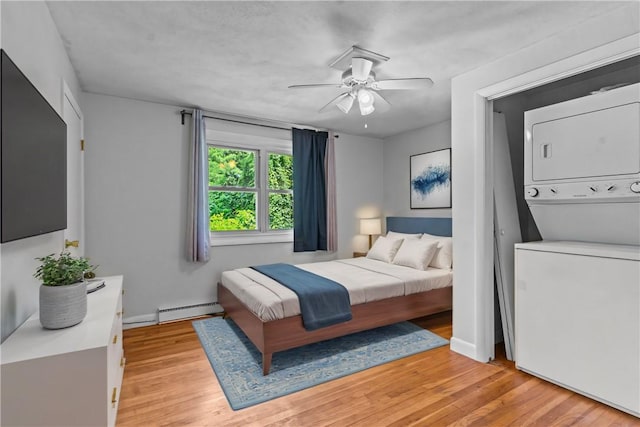 bedroom featuring stacked washer / drying machine, ceiling fan, light wood-type flooring, and baseboard heating