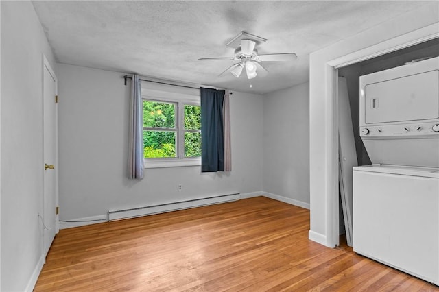 clothes washing area with stacked washing maching and dryer, a textured ceiling, ceiling fan, a baseboard radiator, and light hardwood / wood-style floors