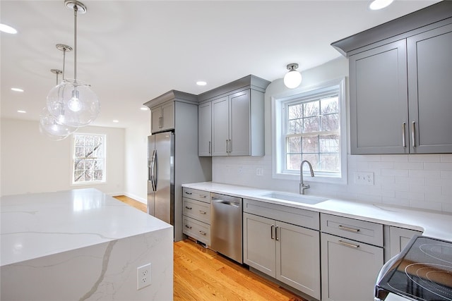 kitchen with gray cabinetry, backsplash, sink, light wood-type flooring, and appliances with stainless steel finishes