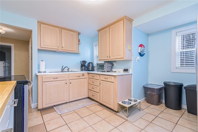 kitchen with stainless steel electric range, light brown cabinets, light tile patterned floors, and sink