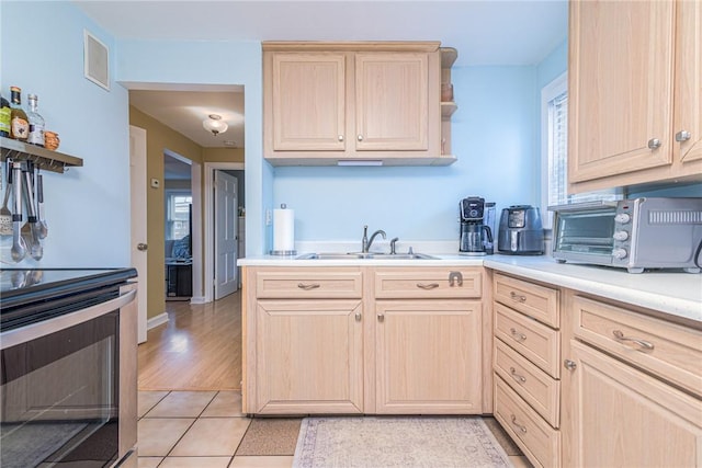 kitchen featuring sink, light brown cabinetry, light tile patterned floors, and range