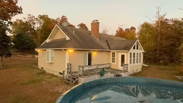 back house at dusk with a wooden deck and a yard