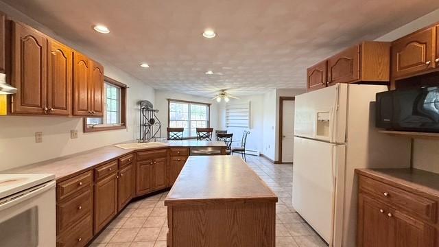 kitchen featuring white appliances, a center island, light tile patterned floors, kitchen peninsula, and ceiling fan