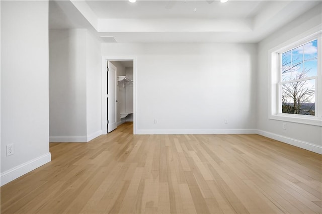 empty room featuring light wood-type flooring and a tray ceiling