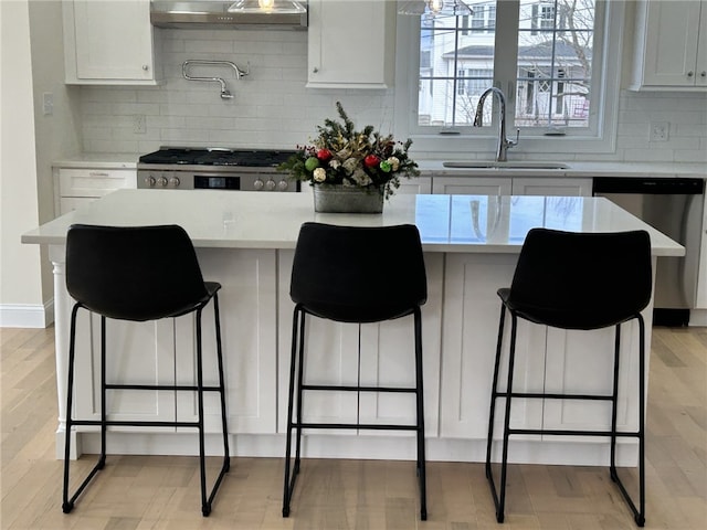 kitchen with a breakfast bar, sink, stainless steel dishwasher, decorative backsplash, and white cabinetry