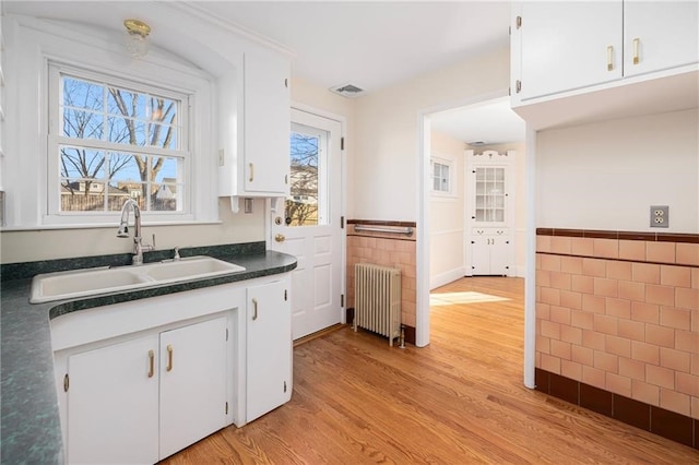 kitchen featuring light wood-type flooring, radiator, sink, tile walls, and white cabinetry