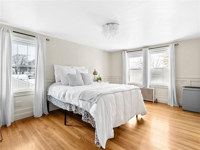 bedroom with radiator, multiple windows, and light hardwood / wood-style floors