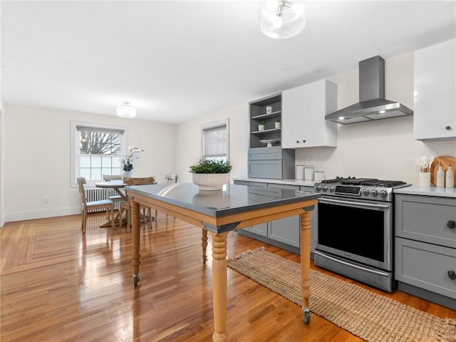 kitchen with stainless steel range with gas cooktop, white cabinets, light wood-type flooring, wall chimney range hood, and gray cabinetry