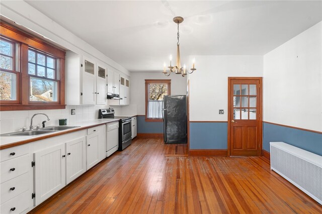 kitchen with black fridge, white cabinetry, hanging light fixtures, stainless steel electric stove, and radiator heating unit