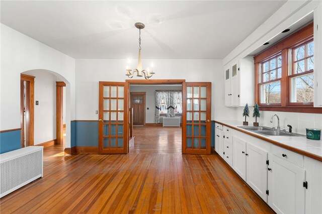 kitchen with pendant lighting, radiator, white cabinetry, french doors, and sink