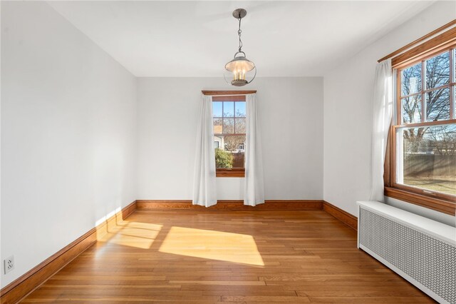 spare room with an inviting chandelier, a wealth of natural light, radiator heating unit, and light hardwood / wood-style floors