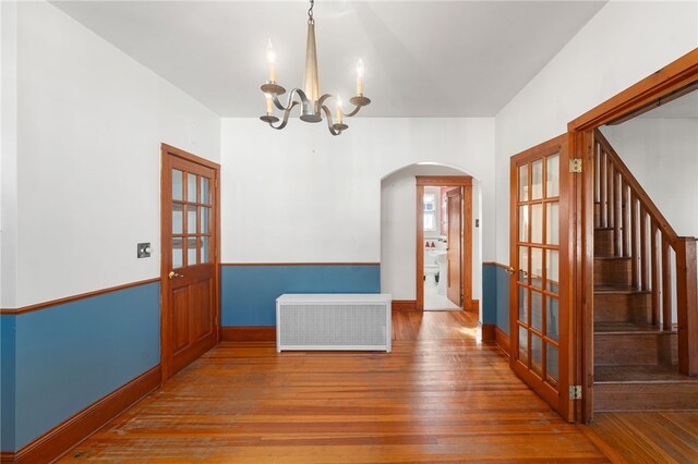 empty room with radiator, a chandelier, hardwood / wood-style flooring, and french doors