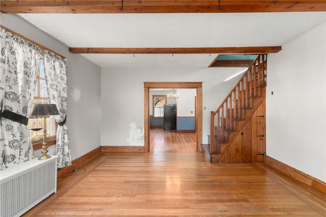 unfurnished room featuring beam ceiling, a notable chandelier, radiator heating unit, and light hardwood / wood-style floors