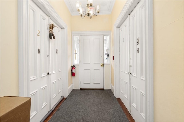 doorway with dark colored carpet, crown molding, and an inviting chandelier