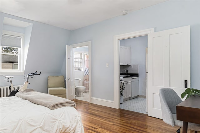 bedroom with ensuite bath, dark hardwood / wood-style flooring, multiple windows, and radiator heating unit