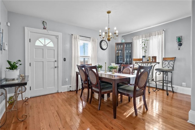 dining space with a baseboard heating unit, light wood-type flooring, a healthy amount of sunlight, and a notable chandelier